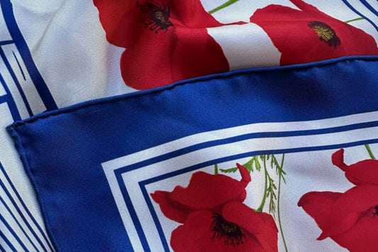 Corner of a silk twill scarf with a red poppy print, navy border and hand-rolled hem