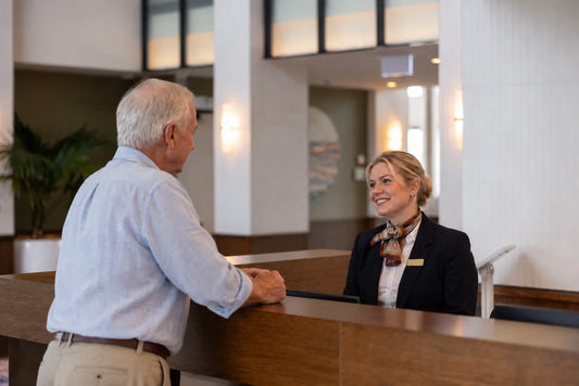 Receptionist at a residential lobby desk wearing a slim brown houndstooth silk satin scarf with an orange and green border, greeting a resident